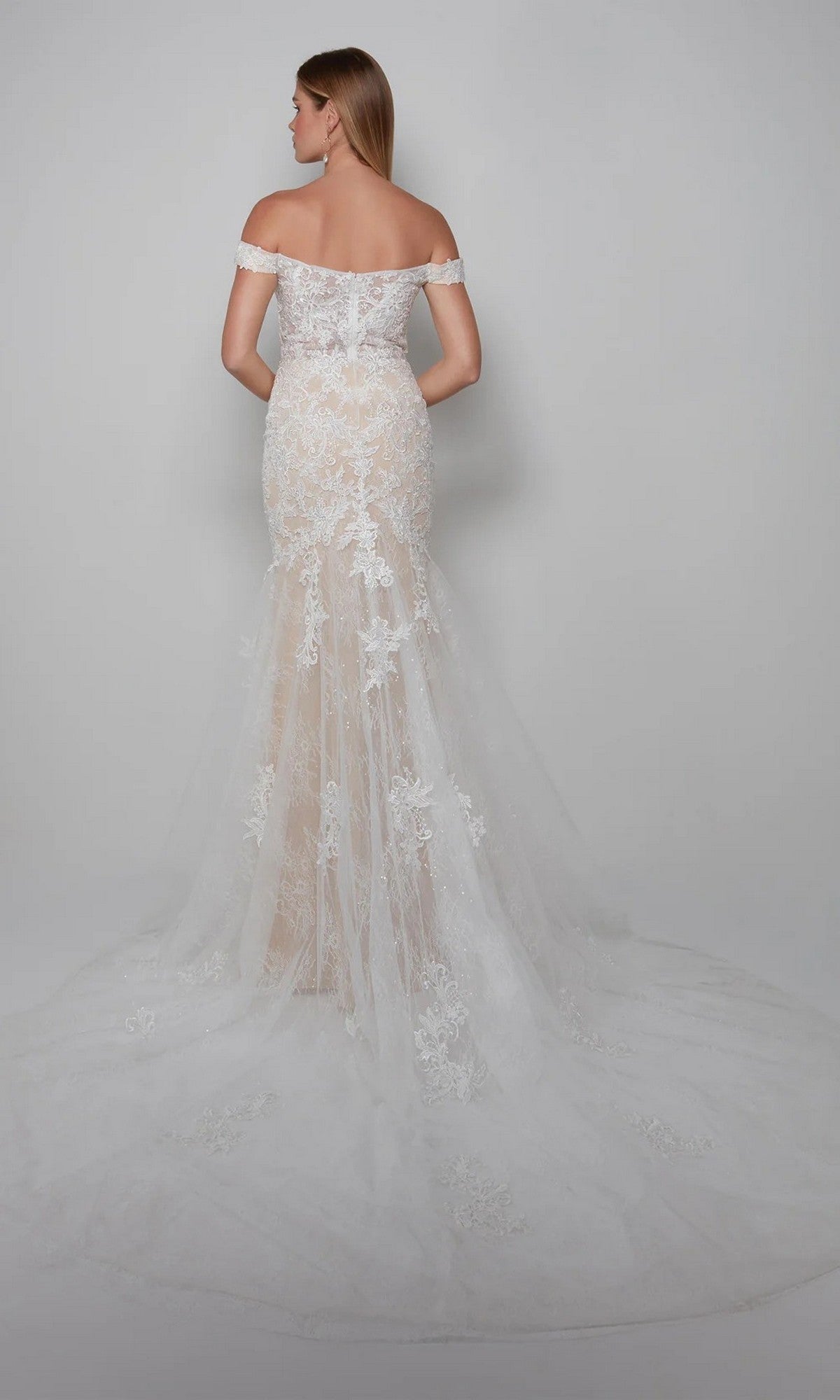 A woman faces away, wearing the Alyce 7086 Long White Dress with floral lace appliques and a sheer train, set against a plain light background.